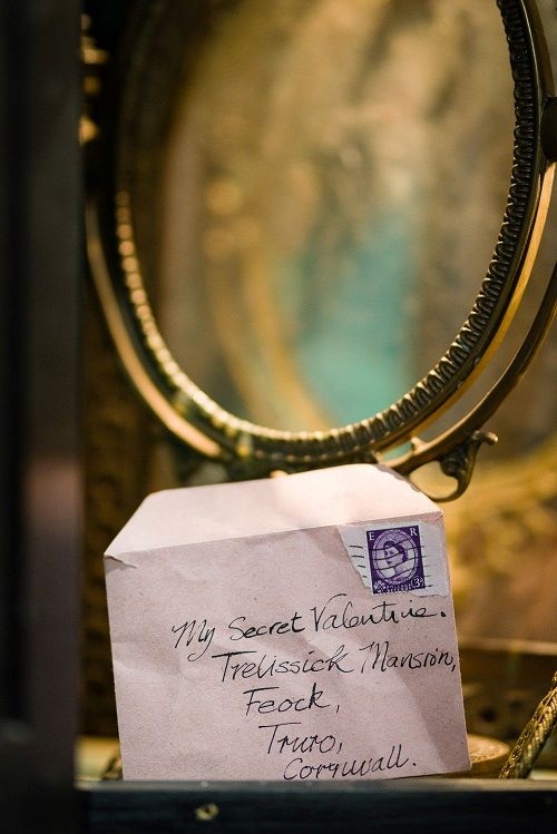 A close-up of a handwritten envelope positioned in front of an ornate antique mirror. The envelope is addressed to "My Secret Valentine, Trelissick Mansion, Feock, Truro, Cornwall" and features a purple postage stamp in the top right corner.